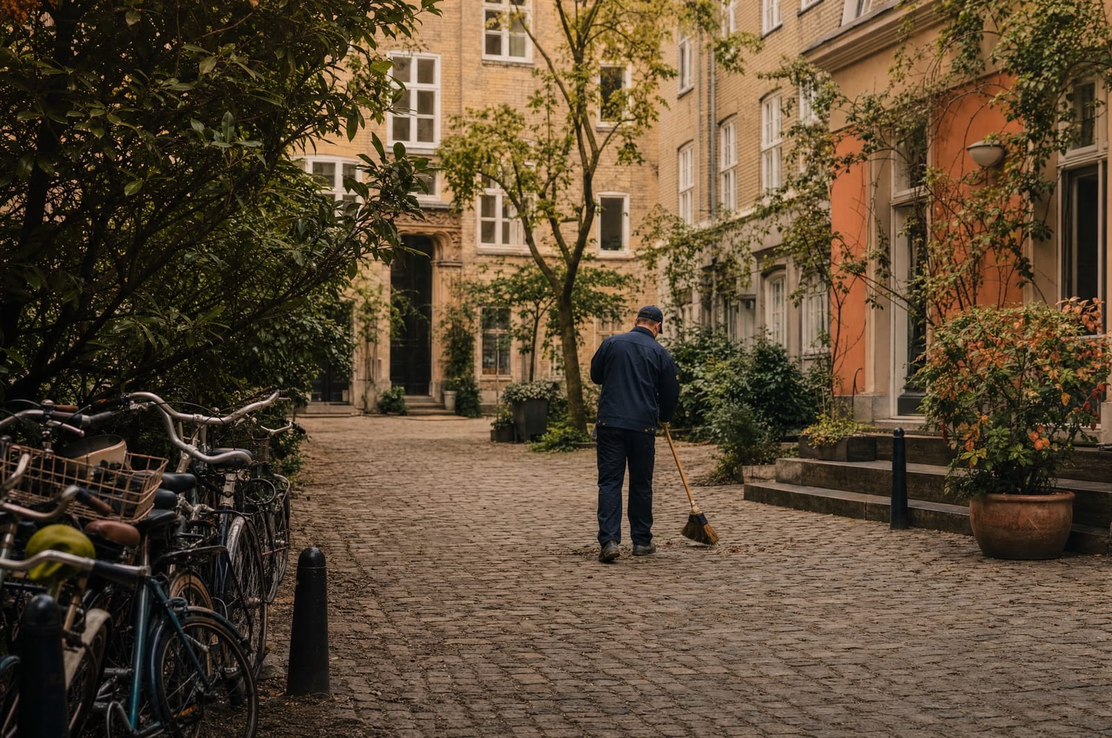 Property caretaker sweeping a cobbled courtyard by a classic Copenhagen building