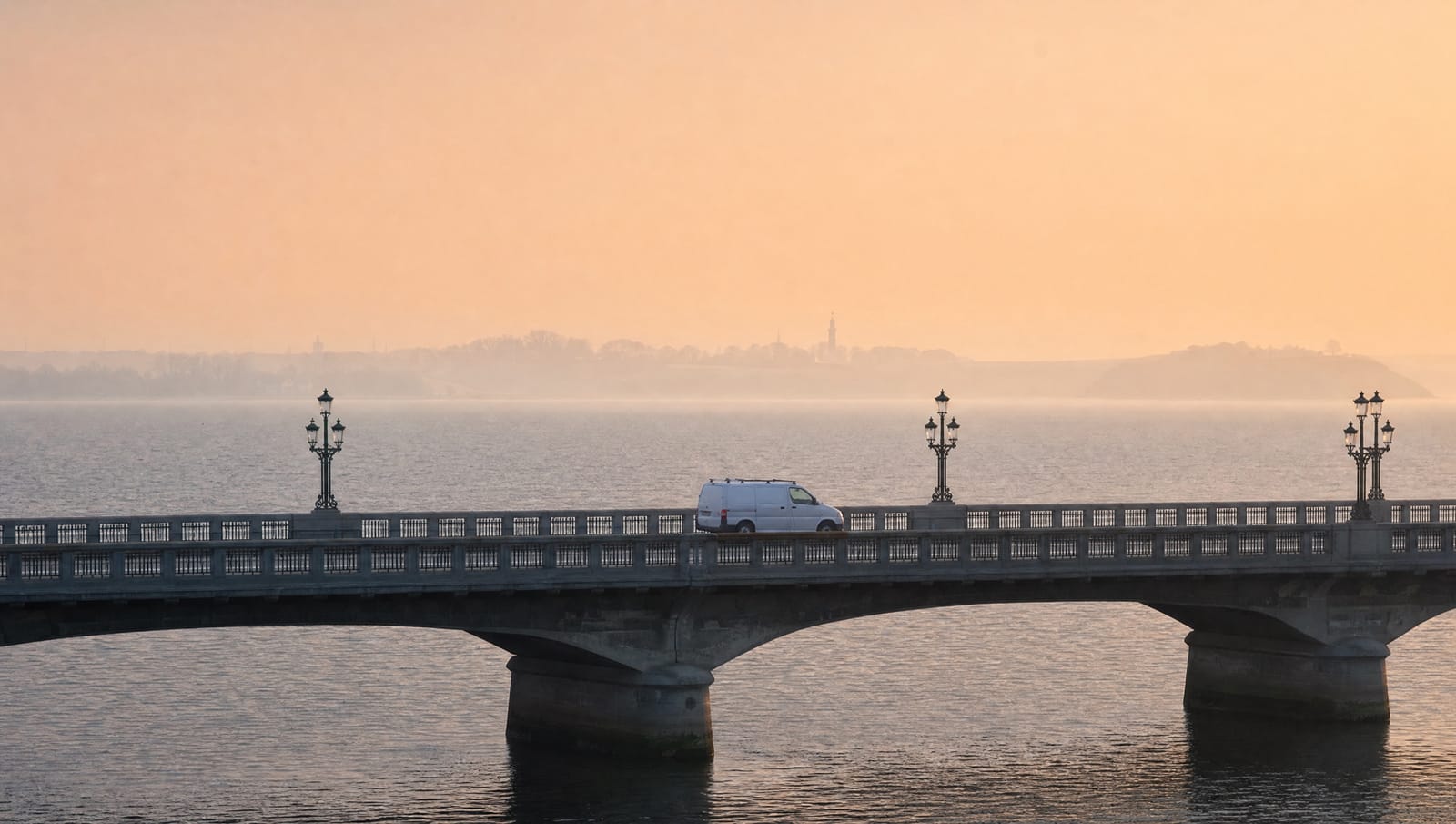 White service van crossing a bridge over calm Danish water at sunrise