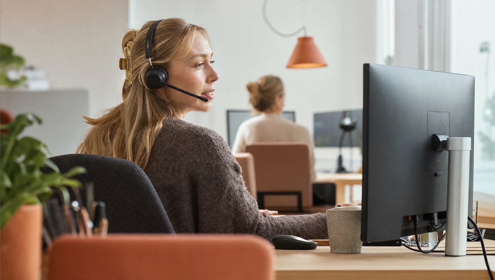 Customer service agent with a headset at a desk in a bright office