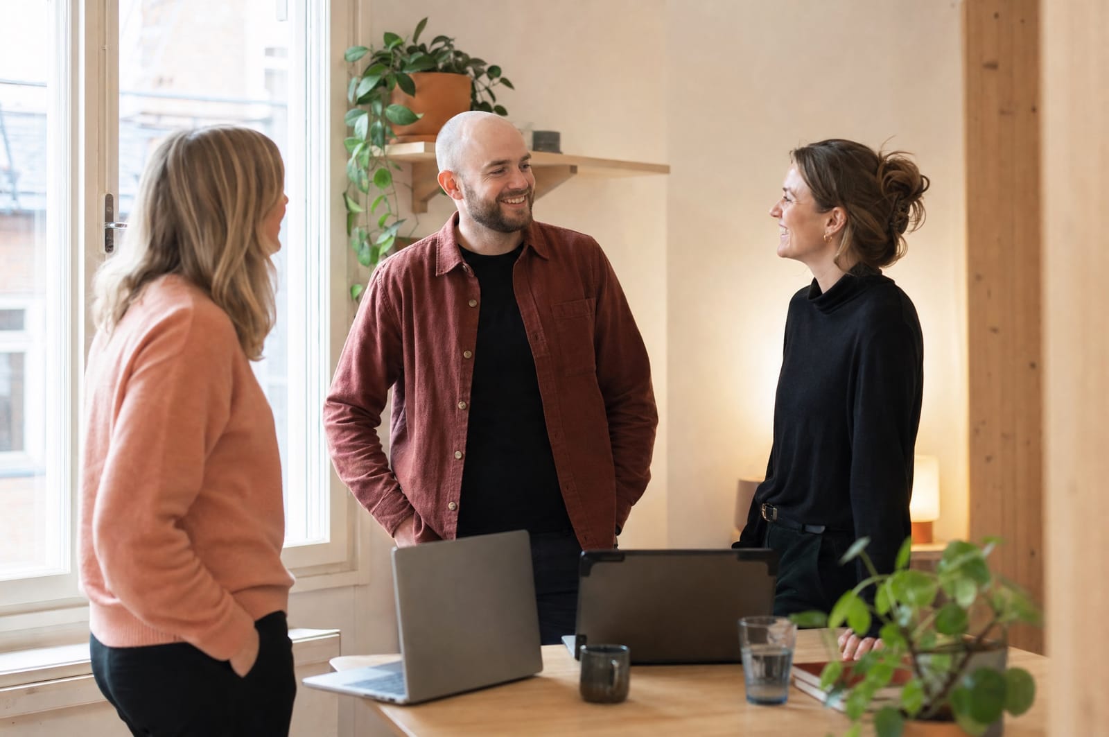 Three colleagues in relaxed conversation at a desk in a bright Scandinavian office